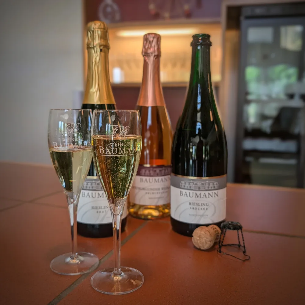 Drei Winzersekte vom Weingut Baumann mit zwei gefüllten Sektgläsern